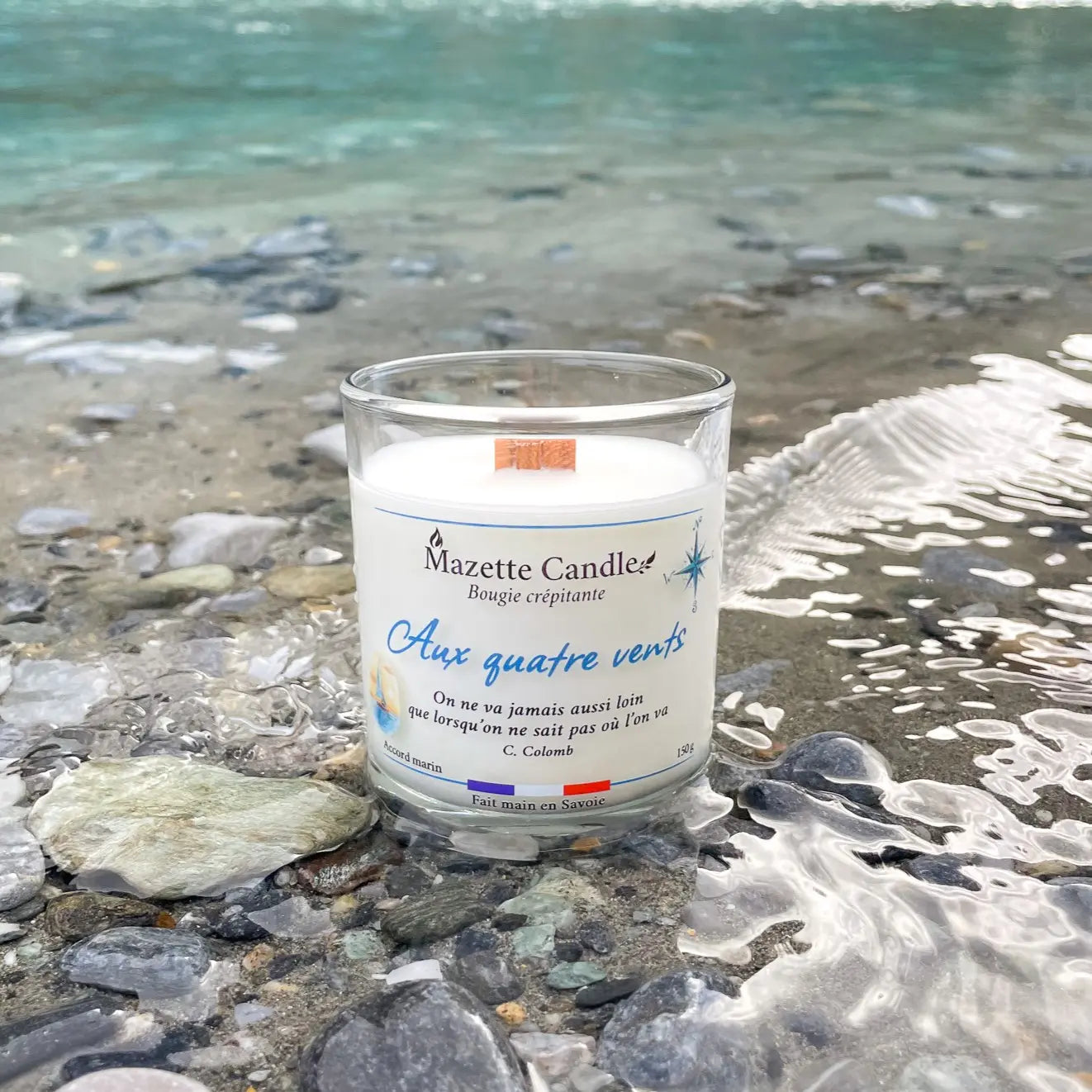 Bougie Mazette Candle Aux quatre vents 150g parfum accord marin, posée dans l’eau au bord d’un ruisseau, petites vagues
