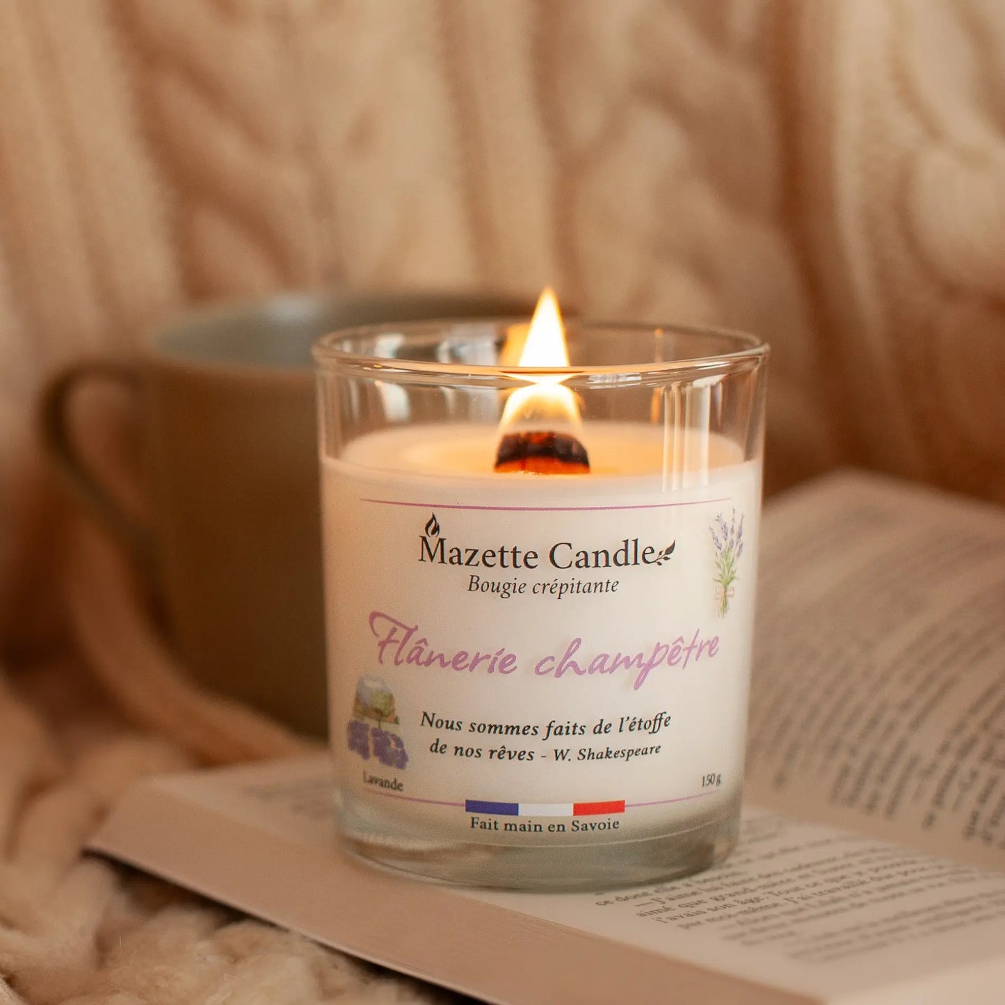 Bougie Mazette Candle Flânerie champêtre 150g parfum lavande, allumée et posée sur un livre dans un décor cocooning