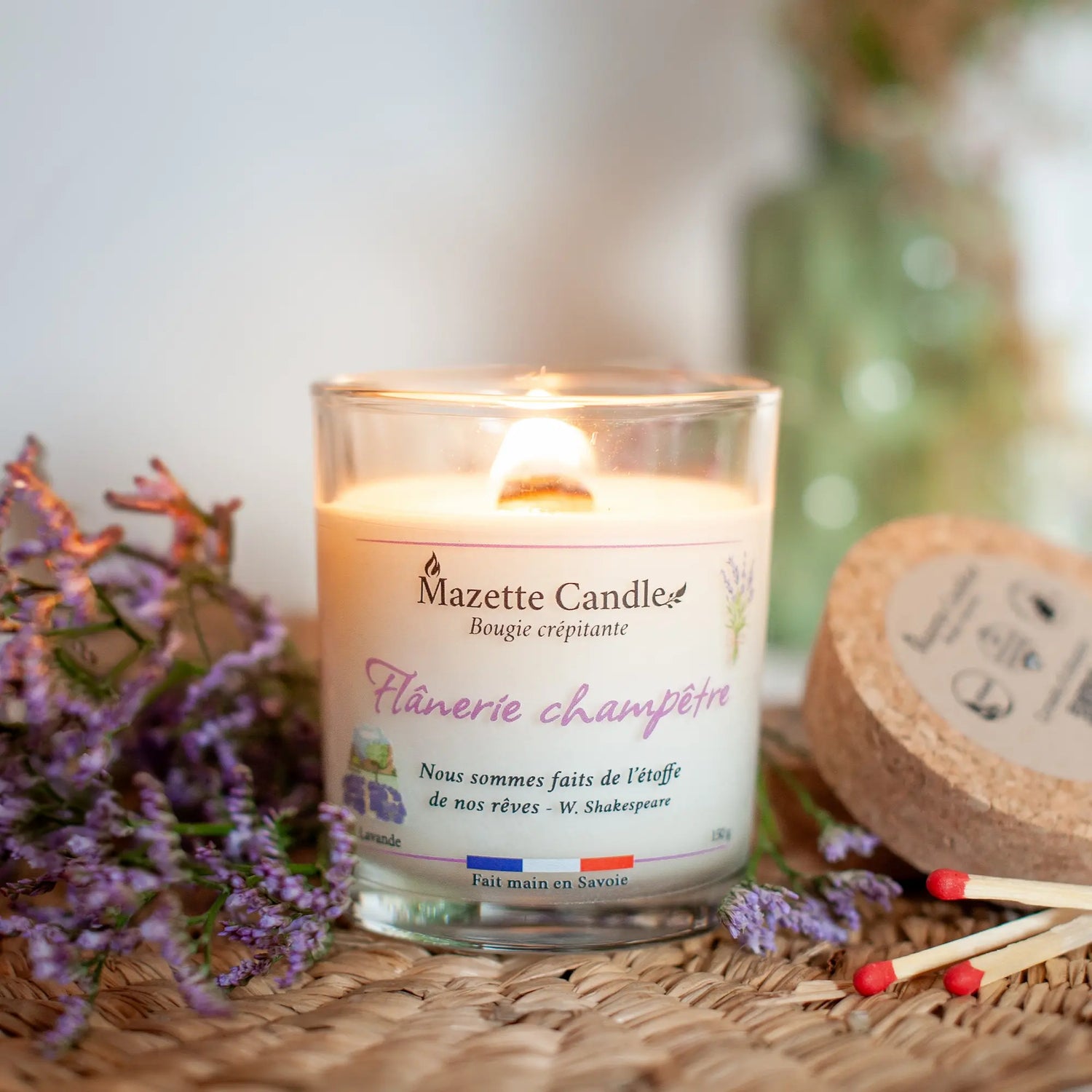 Bougie Mazette Candle Flânerie champêtre 150g parfum lavande, allumée sur un plateau en osier, avec son couvercle en liège