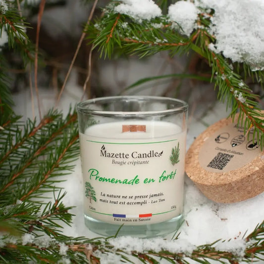 Bougie Mazette Candle Promenade en forêt 150g parfum cèdre, posée sur la neige sous des branches de sapin
