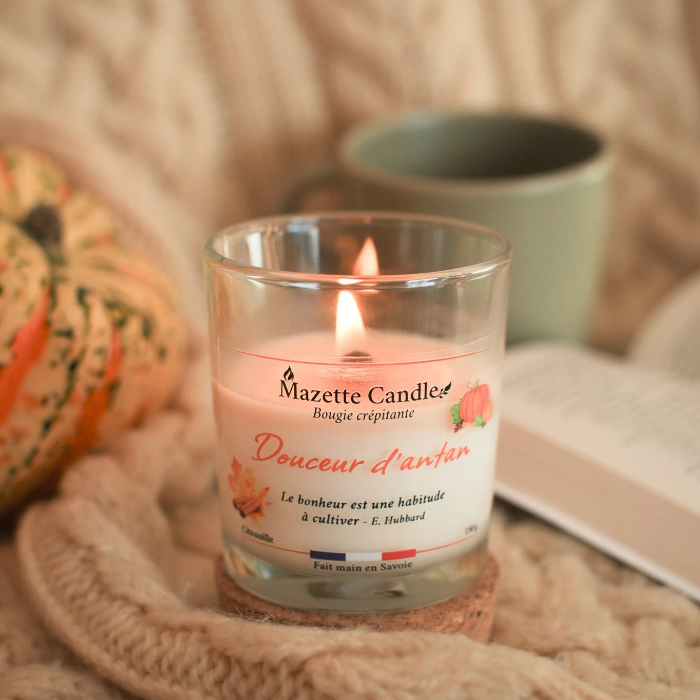 Bougie Mazette Candle Douceur d’antan 150g parfum citrouille, allumée dans un décor cocooning avec courge, mug et livre