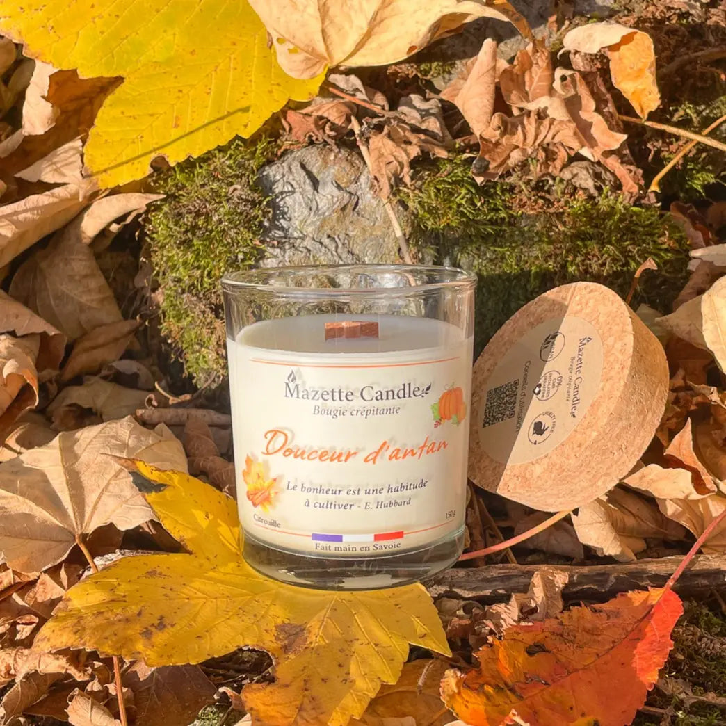 Bougie Mazette Candle Douceur d’antan 150g parfum citrouille, sur des feuilles mortes en forêt, son couvercle en liège à côté