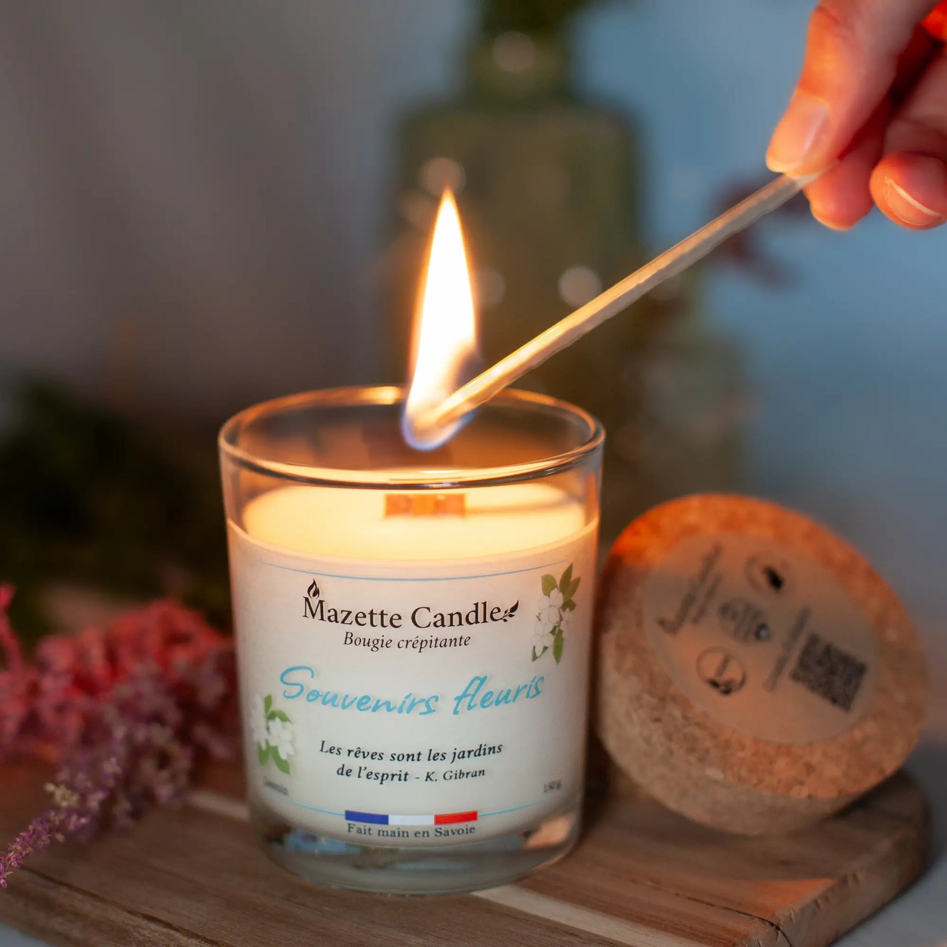 Bougie Mazette Candle Souvenirs fleuris 150g parfum jasmin, en cours d’allumage avec une allumette, couvercle en liège à côté